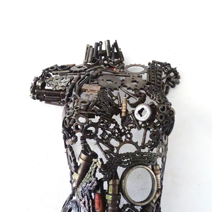 Gros plan sur la poitrine d'un demi-buste féminin en métal recyclé, soudures visibles et textures brutes assemblées à la main