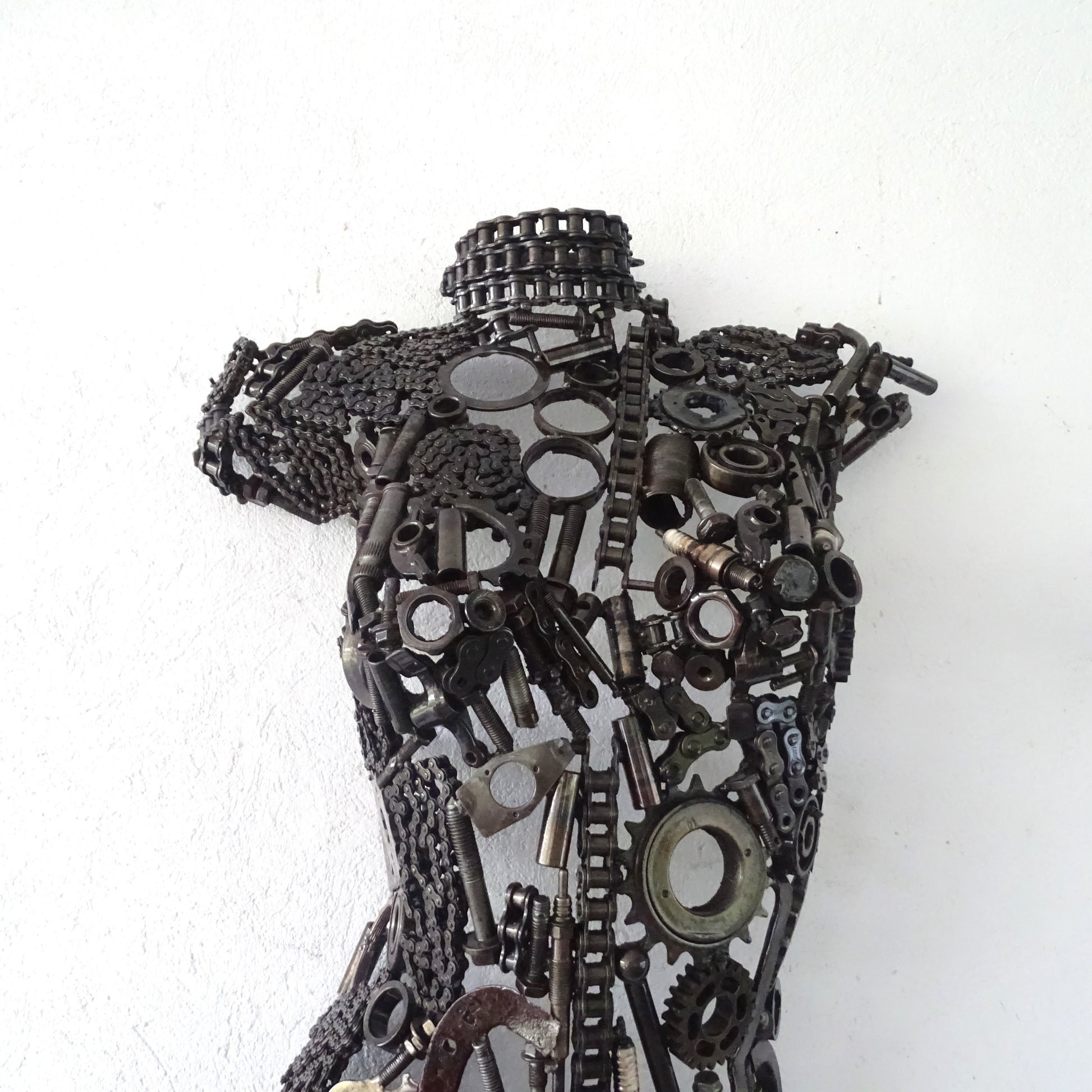 Détail poitrine sculpture femme en métal recyclé avec assemblage artisanal et textures métalliques visibles