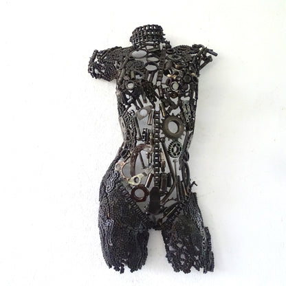 Sculpture demi-buste de femme en métal recyclé installée dans un jardin contemporain près d’un mur texturé