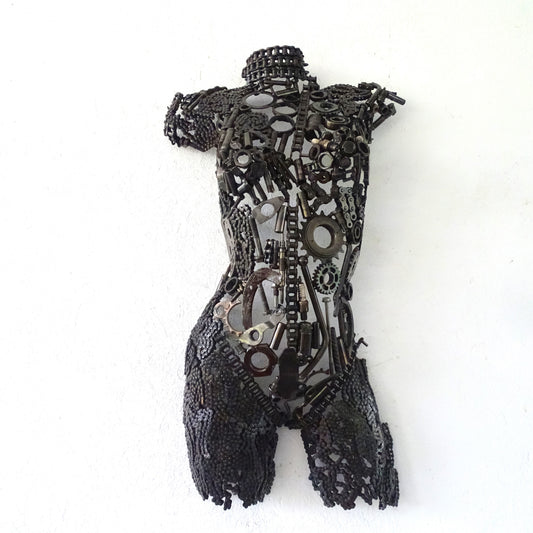Sculpture demi-buste de femme en métal recyclé installée dans un jardin contemporain près d’un mur texturé