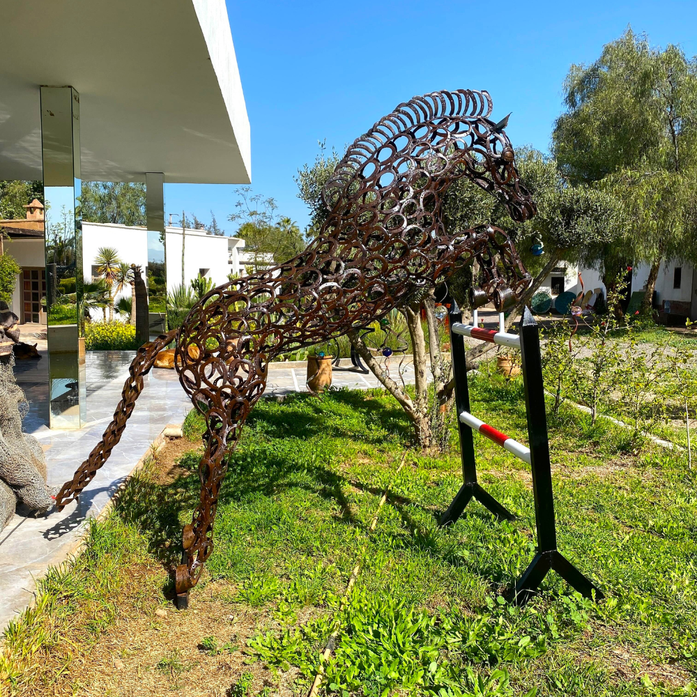 Sculpture cheval saut d’obstacle en fers à cheval recyclés installée dans un jardin contemporain