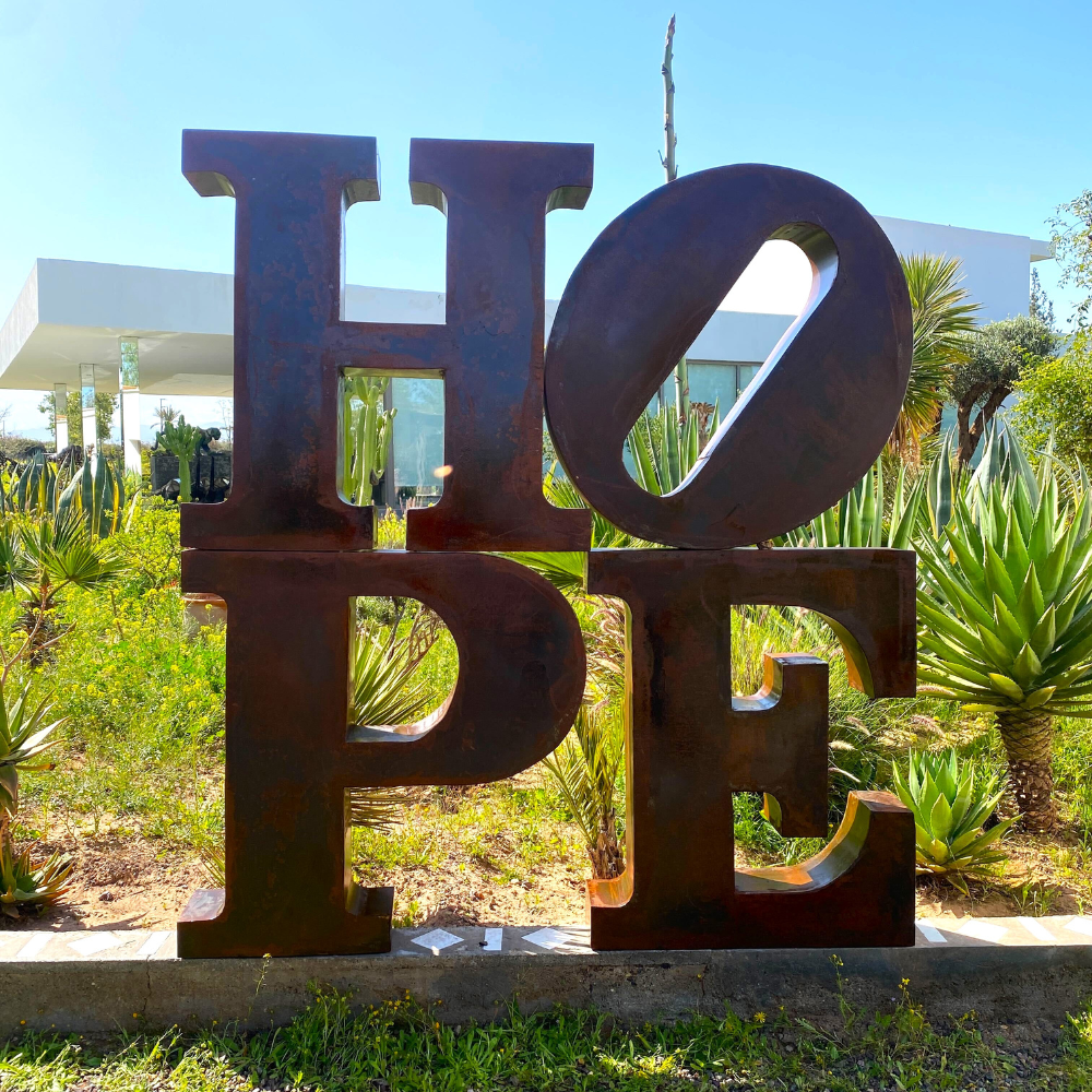 Sculpture "HOPE" en métal oxydé intégrée dans un jardin, finition patinée naturelle et fabrication artisanale, pièce unique.