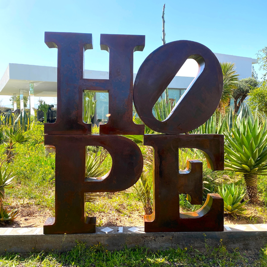 Sculpture "HOPE" en métal oxydé intégrée dans un jardin, finition patinée naturelle et fabrication artisanale, pièce unique.